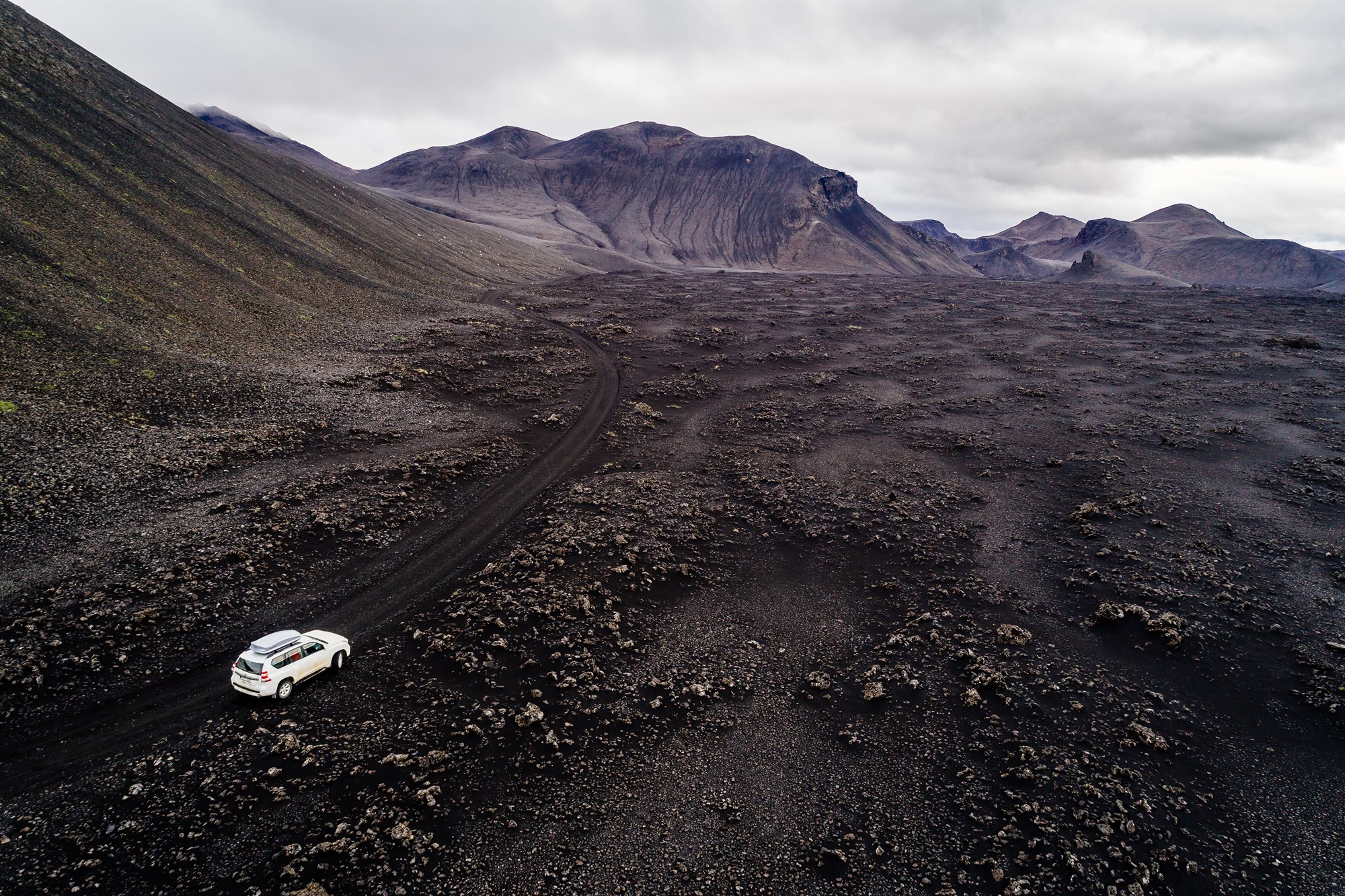 White SUV on Icelandic dirt road near mountain summit