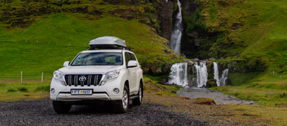 White Toyota Rental SUV and Silver Roof Box with Waterfall and Green Mountain